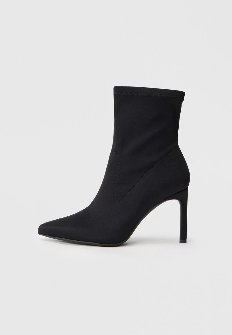 Czarne skarpety w kształcie butów z ostro zakończonym noskiem, na cienkim wysokim obcasie, z elastycznym cholewką sięgającą kostki, na białym tle.