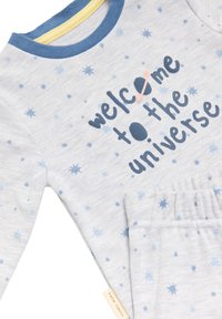 Conjunto de pijama gris claro con patrón de estrellas azules. Presenta un escote de canalé azul y amarillo y el texto "bienvenido al universo" en azul oscuro.