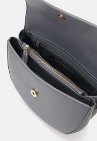 Šedá kožená kabelka s hladkým povrchem, zlatými kovanými detaily, kapsou na zip a magnetickým uzávěrem. Interiér má více přihrádek.