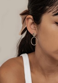Pendientes de tono plateado con un diseño de aro circular y una parte superior redonda con textura. Superficie lisa con una estética minimalista.