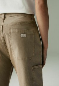 Pantalons khaki avec une coupe slim, fabriqués en coton texturé, présentant une poche arrière avec une petite étiquette et une taille.