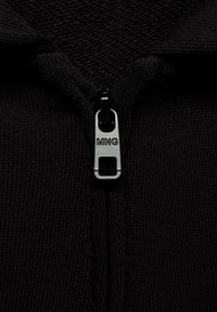 Zwarte zip-up kledingstuk van een gestructureerde stof, met een centrale rits met een zilveren trekker en de merknaam "MNG" zichtbaar op de rits.