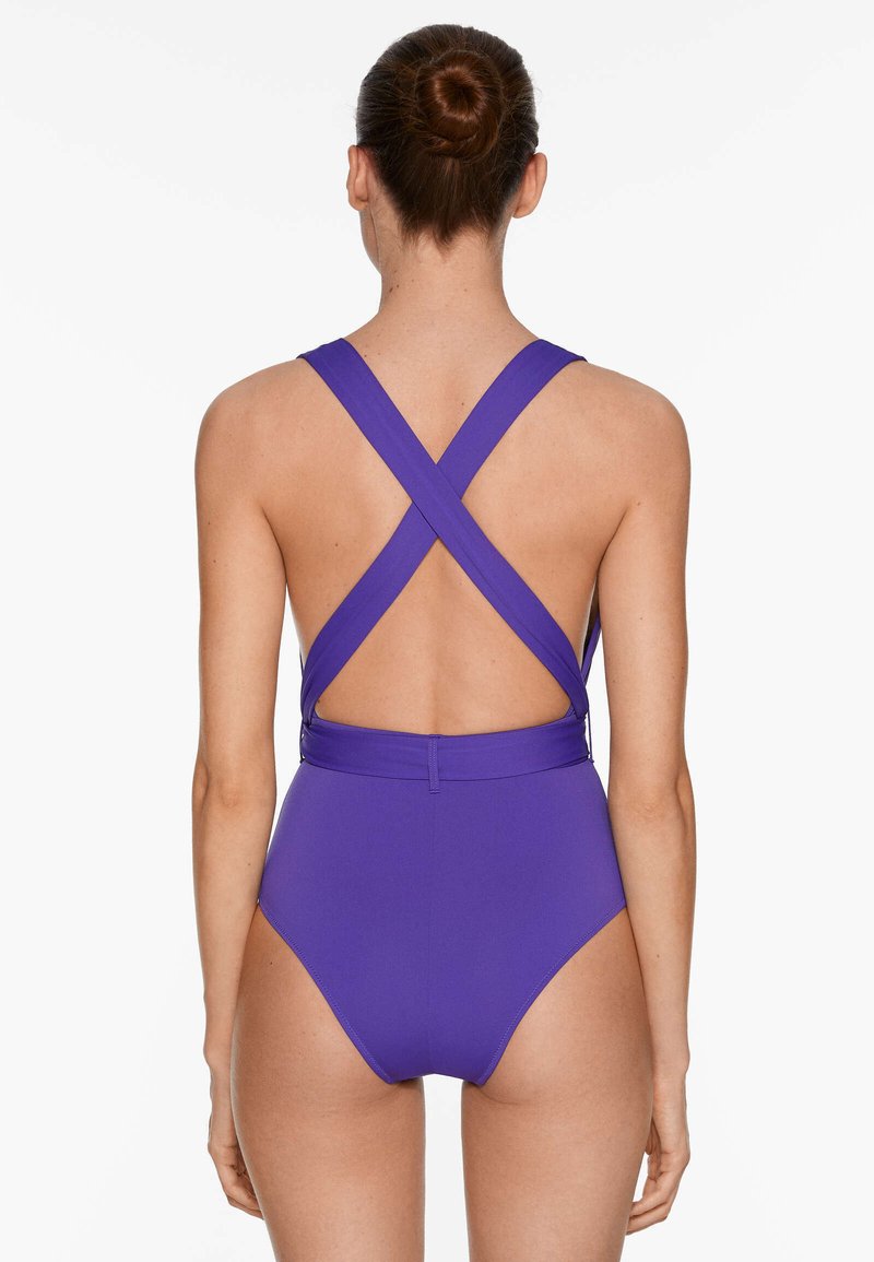 Maillot de bain une pièce violet avec des bretelles croisées au dos, présentant une texture lisse et une coupe haute sur les jambes pour une silhouette élancée.