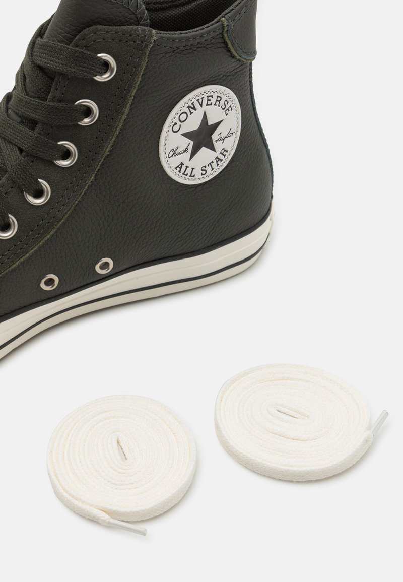 Baskets montantes en cuir noir avec un patch logo circulaire, semelle en caoutchouc blanche et deux lacets ronds blancs en dessous.