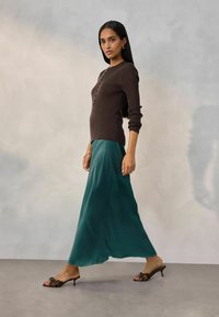 Brun ribbet sweater med knaplukning foran, parret med en flydende teal satin maxi skirt og mønstrede åbne tå mules.