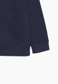 Felpa blu navy realizzata in tessuto con tasca a marsupio, dotata di cuciture rinforzate, polsini a coste e orlo per una maggiore durata.