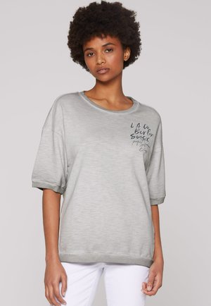 Hellgrau kurzes Sweatshirt mit lässigem Schnitt, featuring umgeschlagenen Ärmeln und einem gestickten Design auf der Vorderseite. Weiche Stofftextur.