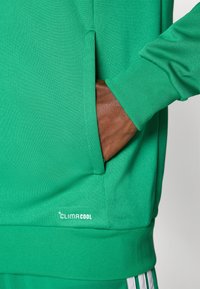 Πράσινο αθλητικό φούτερ με υφασμάτινη επένδυση που επιτρέπει την αναπνοή, ριμπ μανσέτες, πλαϊνή τσ έπη και λογότυπο CLIMACOOL στο κάτω αριστερό μέρος.