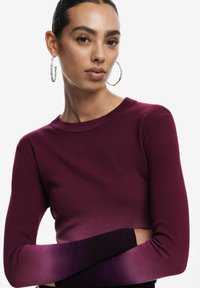 Top lungo borgogna con maniche, dal collo rotondo, caratterizzato da una sfumatura viola sui polsini. Tessuto a maglia morbido con design aderente.