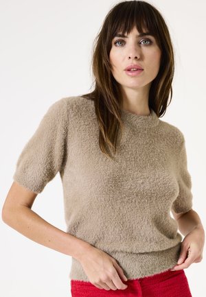 Pull beige à manches courtes en texture fluffy, avec un col rond et une coupe légèrement cropped, associé à un pantalon rouge texturé.