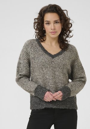 Pull en tricot gris et beige avec un col en V, texture épaisse et poignets côtelés. Présente une coupe ample et un ourlet ondulé.