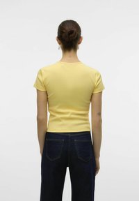 T-shirt gialla aderente a maniche corte, con texture a costine e orlo dritto, abbinata a jeans blu scuri con tasche posteriori.