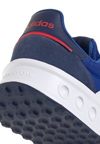 Talons de basket Adidas bleus avec bande rouge, semelle blanche amortissante embossée du mot « CLOUDFOAM » et semelle à motif hexagonal.