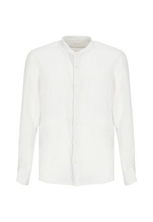 Uomo che indossa una camicia bianca a maniche lunghe abbottonata e pantaloncini bianchi fino al ginocchio, in piedi con espressione neutra su uno sfondo semplice.