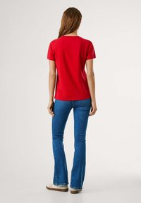 T-shirt rouge à manches courtes avec col rond, associé à un jean flare bleu. Tissu lisse et style ajusté, vu de dos.