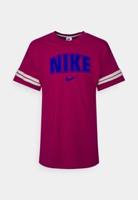 Fuchsiové tričko s velkým modrým logem "NIKE", bílými pruhy na rukávech, kulatým výstřihem a volným střihem.