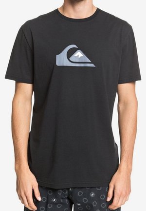 Mężczyzna w czarnej koszulce z szarym logo fali i góry na piersi, w połączeniu z czarnymi szortami z małymi wzorami słońca.