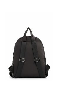 Mochila de nylon negra con frente acolchado, dos asas superiores, correa ajustable y herrajes en tono plateado. Cuenta con un cierre con cremallera y textura suave.