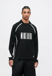 Svart hettegenser med "NIKE AIR" i hvit skrift, med hette, som har hvite sidepaneler og ribbestrikkede mansjetter. Laget av mykt stoff.