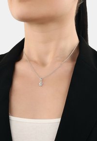 Collana in argento con un piccolo pendente a forma di elefante, indossata sopra una maglietta di colore chiaro e sotto un giubbotto scuro.