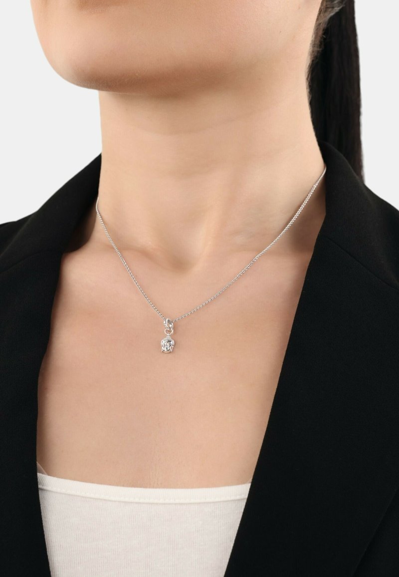 Collana in argento con un piccolo pendente a forma di elefante, indossata sopra una maglietta di colore chiaro e sotto un giubbotto scuro.