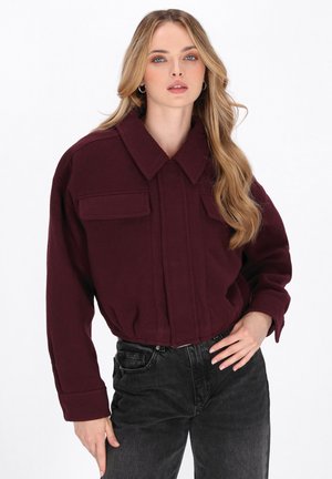 Burgunderfarbene, cropped Jacke mit großem Kragen, zwei Brusttaschen und langen Ärmeln. Kombiniert mit hoch taillierten schwarzen Jeans. Weiche Textur.