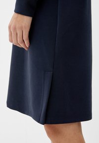 Mörkblå klänning med en slät textur, med en sidoöppning och prydlig sömnad, som visar en enkel och modern design.