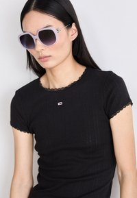 Svart ribbet topp med korte ermer og blondekant, kombinert med overdimensjonerte lyse lilla solbriller med gradientlinser og metalliske detaljer.