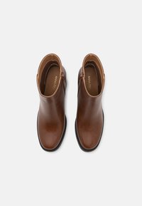 Botas de tobillo de cuero marrón con un acabado suave, punta redondeada y cremallera lateral. Suela de goma negra y forro interior suave.