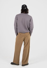 Grauer übergroßer Sweatshirt mit geripptem Saum, kombiniert mit braunen weiten Hosen. Schwarze Mütze mit Logo und Stiefel mit dicker Sohle.