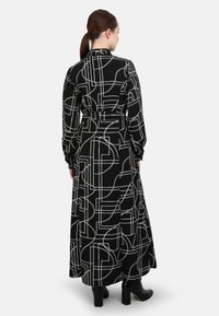 Long black dress with white geometric patterns, featuring a high collar, long sleeves, and a tie waist. Textured, flowing fabric with a skirt.