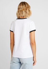 Vit bomull t-shirt med svart ribbad krage och ärmslut, med en klassisk passform och slät textur. Bakre vy visas.