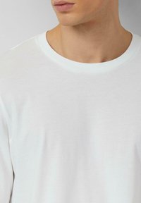 Weißes T-Shirt mit Rundhalsausschnitt aus Baumwolle, mit glatter Textur und minimalistischem Design. Der Kragen hat einen weißen Akzent entlang der Kante.