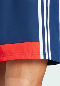 Pantalones cortos azul marino con un dobladillo rojo, que presentan tres franjas blancas a lo largo del costado. Fabricados con un tejido ligero y texturizado para mayor comodidad.