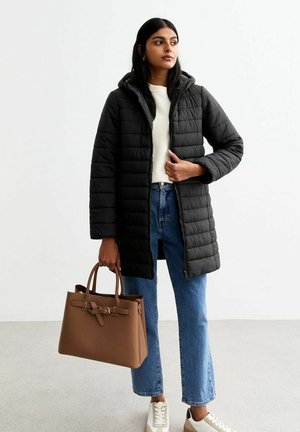 Black puffer jacket with a hood, zipper front, worn over a light sweater and blue high-waisted jeans. Holding a brown handbag and wearing white sneakers.