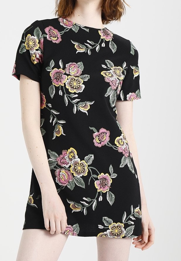 Femme portant une robe noire à manches courtes avec des motifs floraux roses, jaunes et verts.