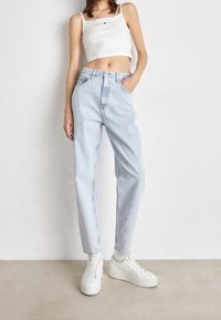 Ljust blå högmidjade jeans med rak passform, kombinerat med en vit kortärmad tanktopp och vita sneakers. Minimalistisk design, avslappnad stil.