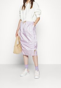 Falda lilada, ligera y fruncida, con bolsillos laterales y detalle de cordón. Combinada con una sudadera blanca corta y zapatillas de colores pastel.