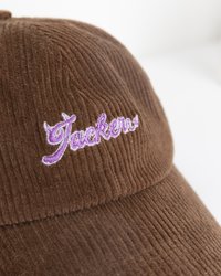 Braune Kordmütze mit gesticktem lila "Jackens" Schriftzug auf der Vorderseite. Die Textur ist gestreift und bietet ein weiches Gefühl.