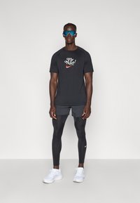 Fekete, nedvességgel elvezető póló "Fly Nike!" grafikával, szürke rövidnadrággal és fekete leggingssel párosítva. Fehér sportcipők teszik teljessé a megjelenést.