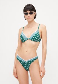 Žalias bikini rinkinys, puošiamas gėlių raštu, nėrinių apdaila ir trikampio formos liemenėlės dizainu su reguliuojamomis petnešėlėmis; prigludę, žemo juosmens bikini apatiniai.