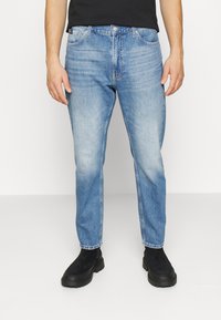 Lichtblauwe denim jeans met een vervaagd effect, rechte pijpen, vijf zakken en een knoopsluiting, gecombineerd met zwarte enkellaarsjes.