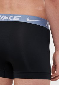 Crne bokserice s mekim, elastičnim svijetloplavim pojasom s bijelim "Nike" logom. Glatka tekstura, srednji kroj.
