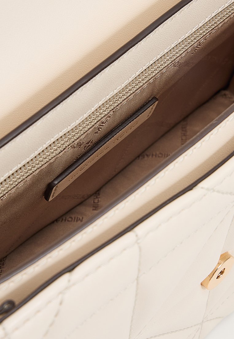 Innenseite einer cremefarbenen Lederhandtasche mit einem braunen Futter, einem Kartenfach, einem Reißverschlussfach und einem Akzent aus goldfarbener Hardware.