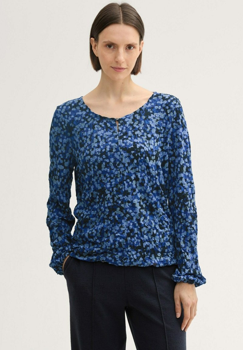 Bluse mit Blumenmuster in Blau, runder Ausschnitt, langen Ärmeln und gerafften Bündchen. Leichter Stoff mit verschiedenen Blautönen auf schwarzem Hintergrund.