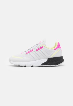 Des baskets blanches avec une tige en toile texturée, ornées d'accents roses et jaunes, de trois rayures sur le côté et d'une semelle en caoutchouc noire.