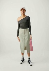 Pilkas off-shoulder topas, aukštu liemeniu šviesiai žalias sijonas su priekine skeltimi, juodi sportbačiai ir rožinė rankinė. Sklandžios tekstūros, laisvalaikio dizainas.