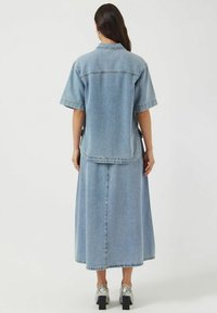 Completo in denim con una camicia azzurra chiara e una gonna lunga a taglio dritto. Scarpe nere con tacco a blocco e dettagli in stampa serpente.