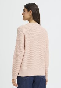 Ljusrosa stickad tröja med ribbad textur och diamantmönster. Har rundad halsringning och långa ärmar med en avslappnad passform.