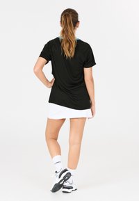 Svart atletisk t-shirt med korta ärmar och en blå accentkrage, tillsammans med en vit tenniskjol. Modellen har på sig vita sneakers och strumpor.